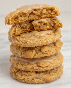 Stack of iced cinnamon brown sugar oatmeal cookies with vanilla glaze dripping down the sides on white plate